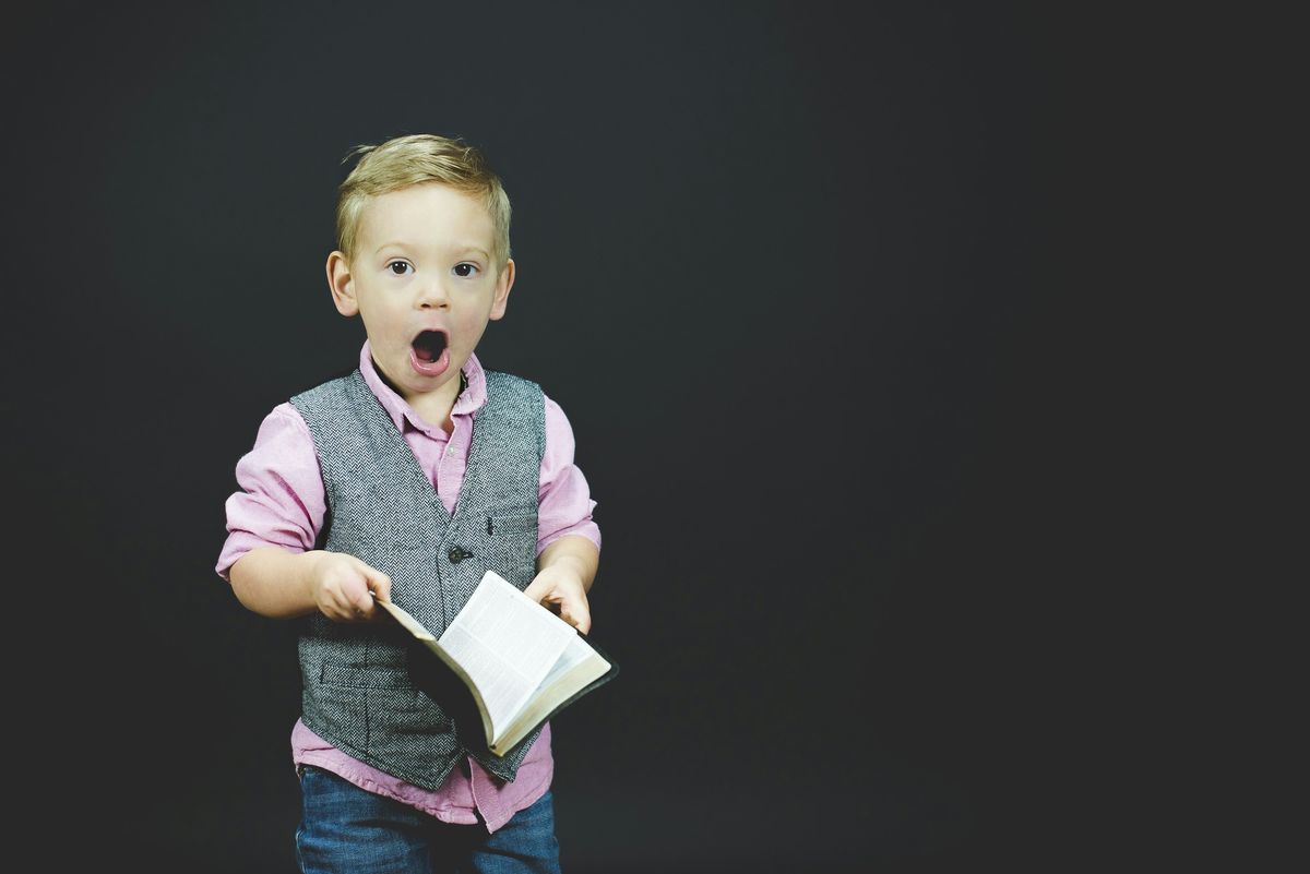 Surprised, dapper boy holding a book on a dark background